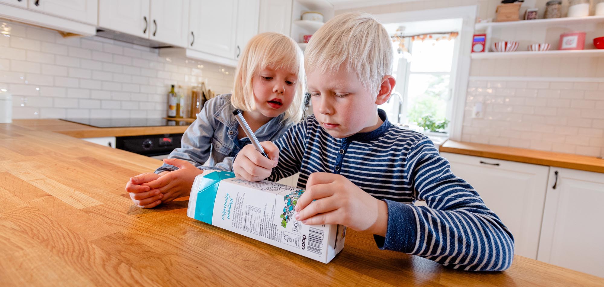 Jente på fire og gutt på åtte år skriver navn på melkekartongen.