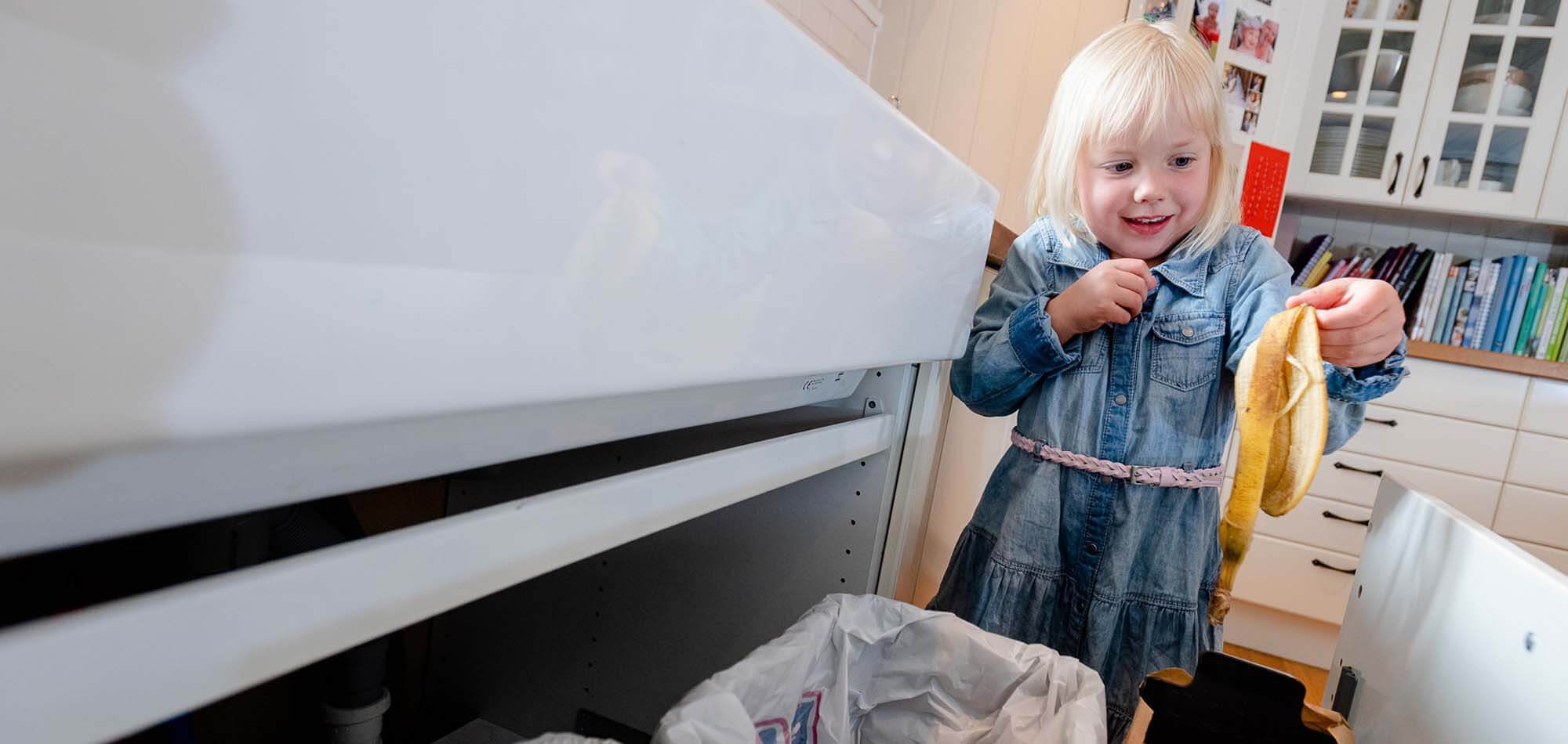 Liten jente kaster bananskall i matavfallet.