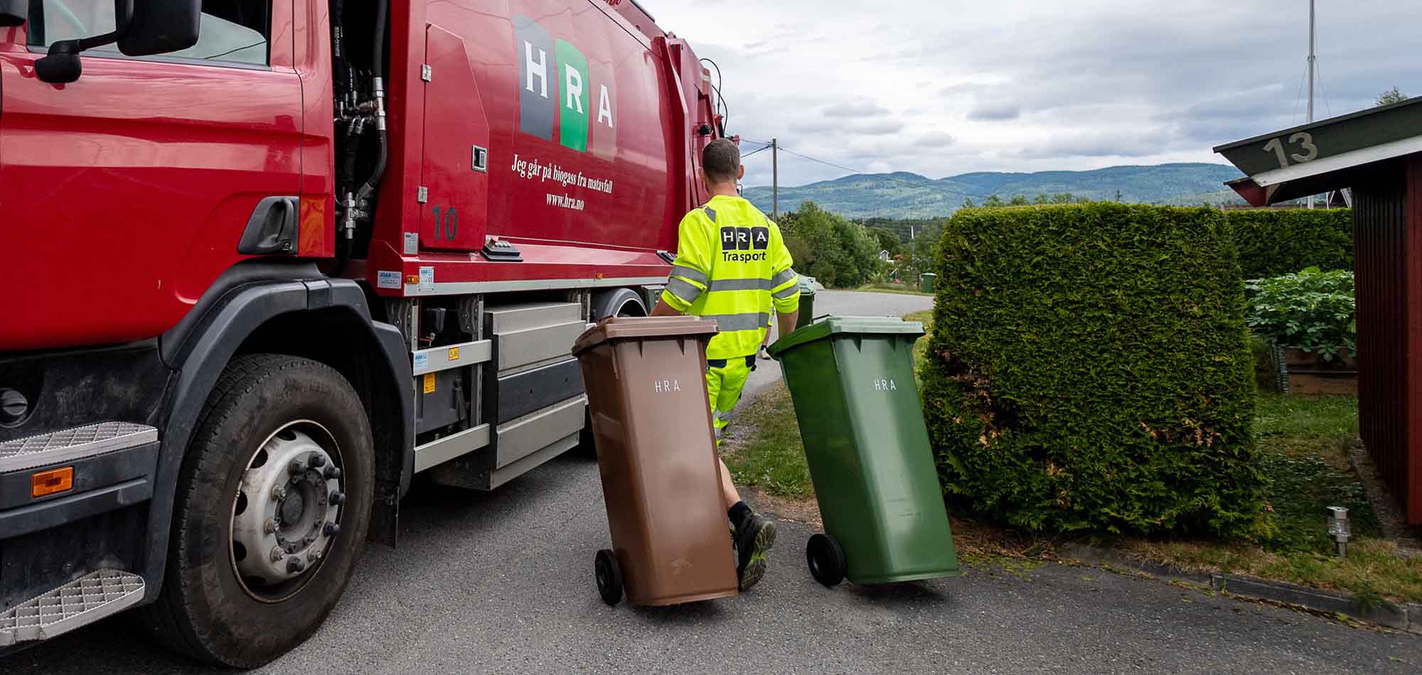 Renovatør triller grønn og brun dunk til rød renovasjonsbil fra HRA.